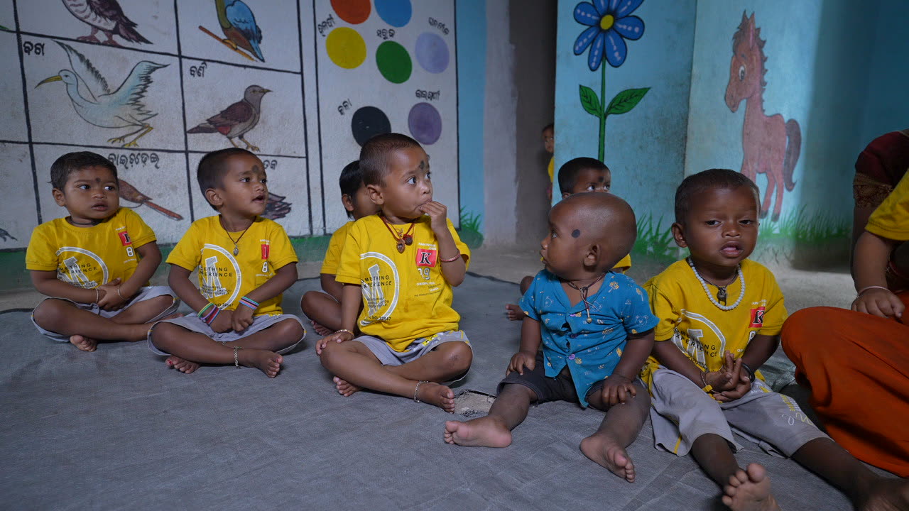 Row of anganwadi children in yellow t-shirts in front of a painted mural
