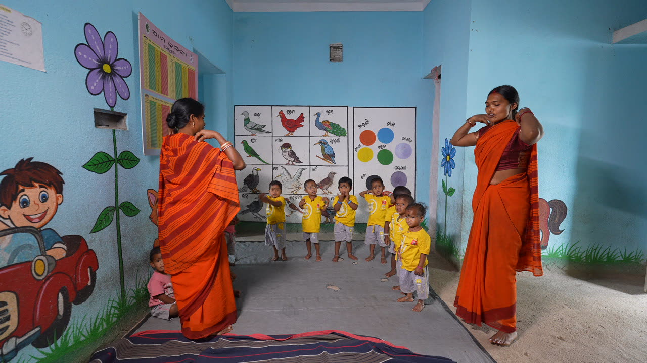 Anganwadi teachers leading a line of toddlers through an activity