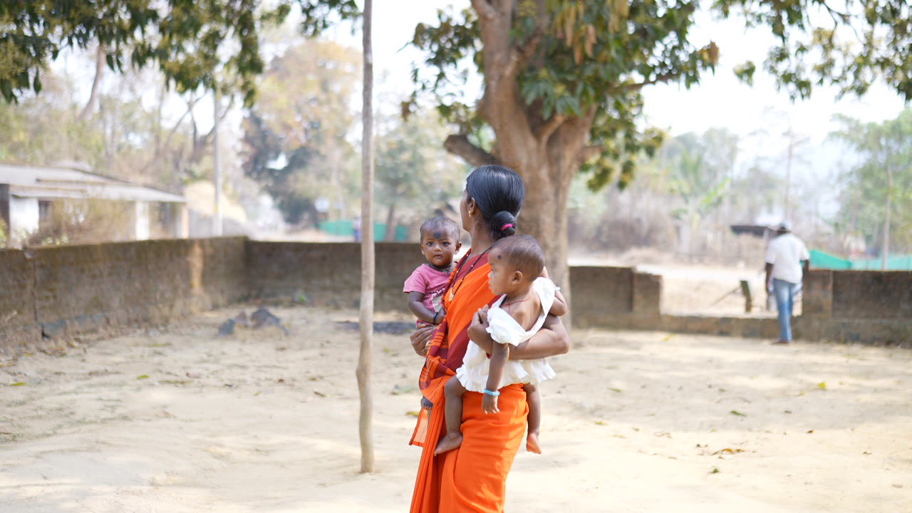 An anganwadi worker carrying two toddlers across the village ground