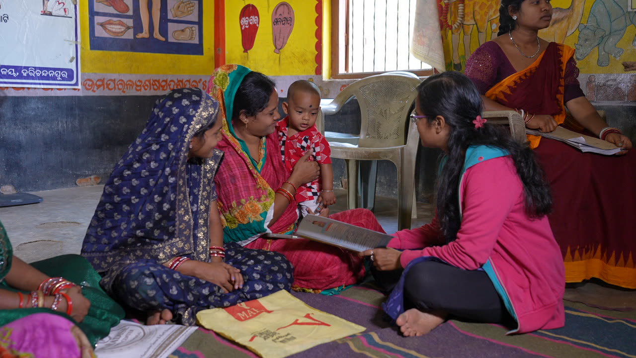 A field worker guiding a mother and her baby through a home activity on the floor