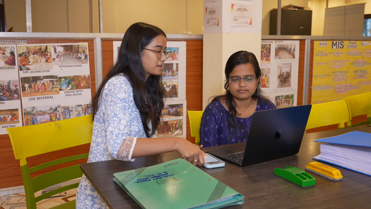 Studio colleague showing something on a phone to a seated team member at the project office